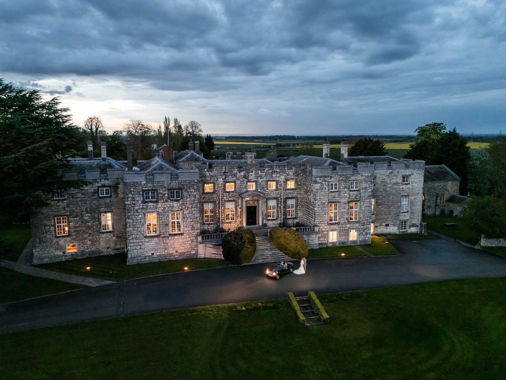 drone photo at dusk of Hazlewood Castle with new-le-weds stood in front of of the castle
