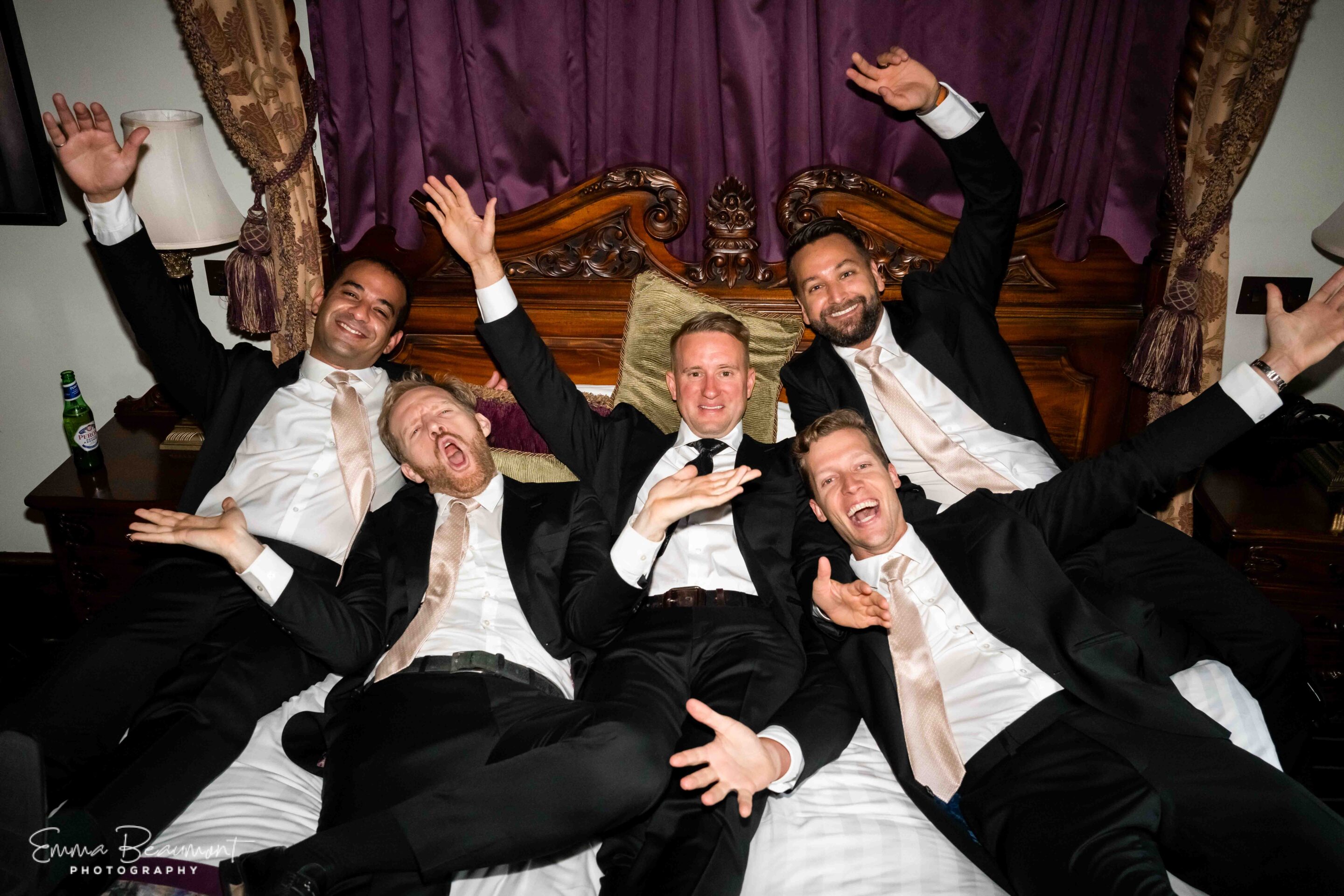 groomsmen lie on bridal bed cheering at Peckforton Castle