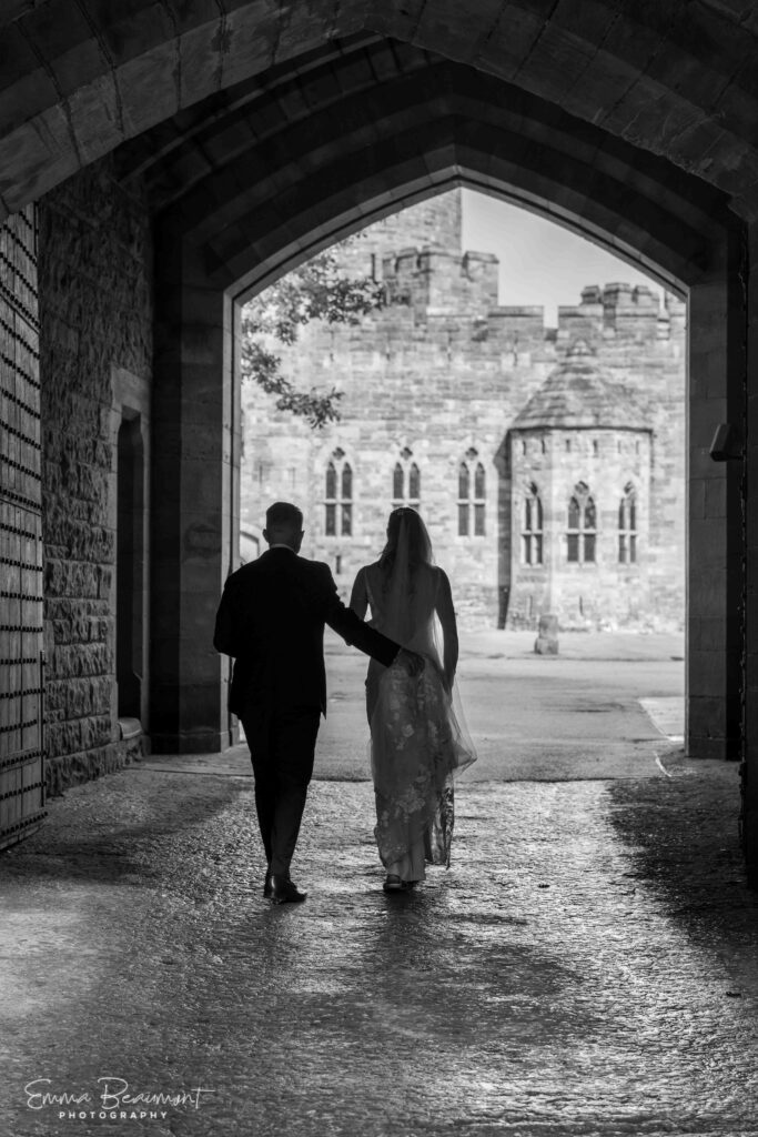 couple walk through archway of Peckforton Castle