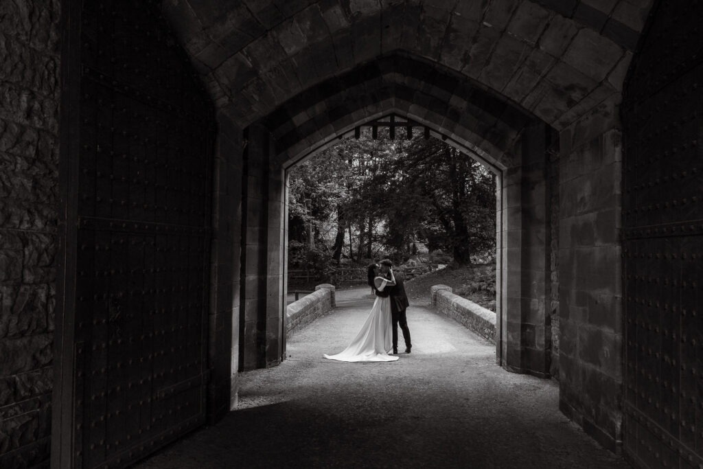 couple kiss in archway of Peckforton Castle