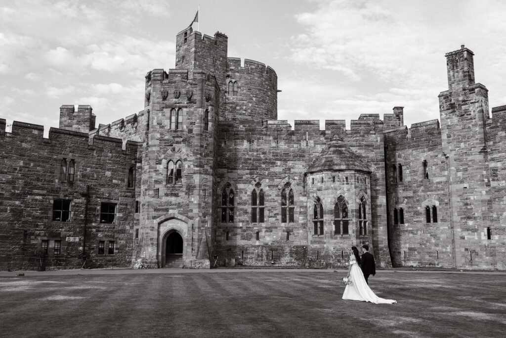 brides and groom walk across grass at the front of Peckforton Castle in Tarporley, Cheshire
