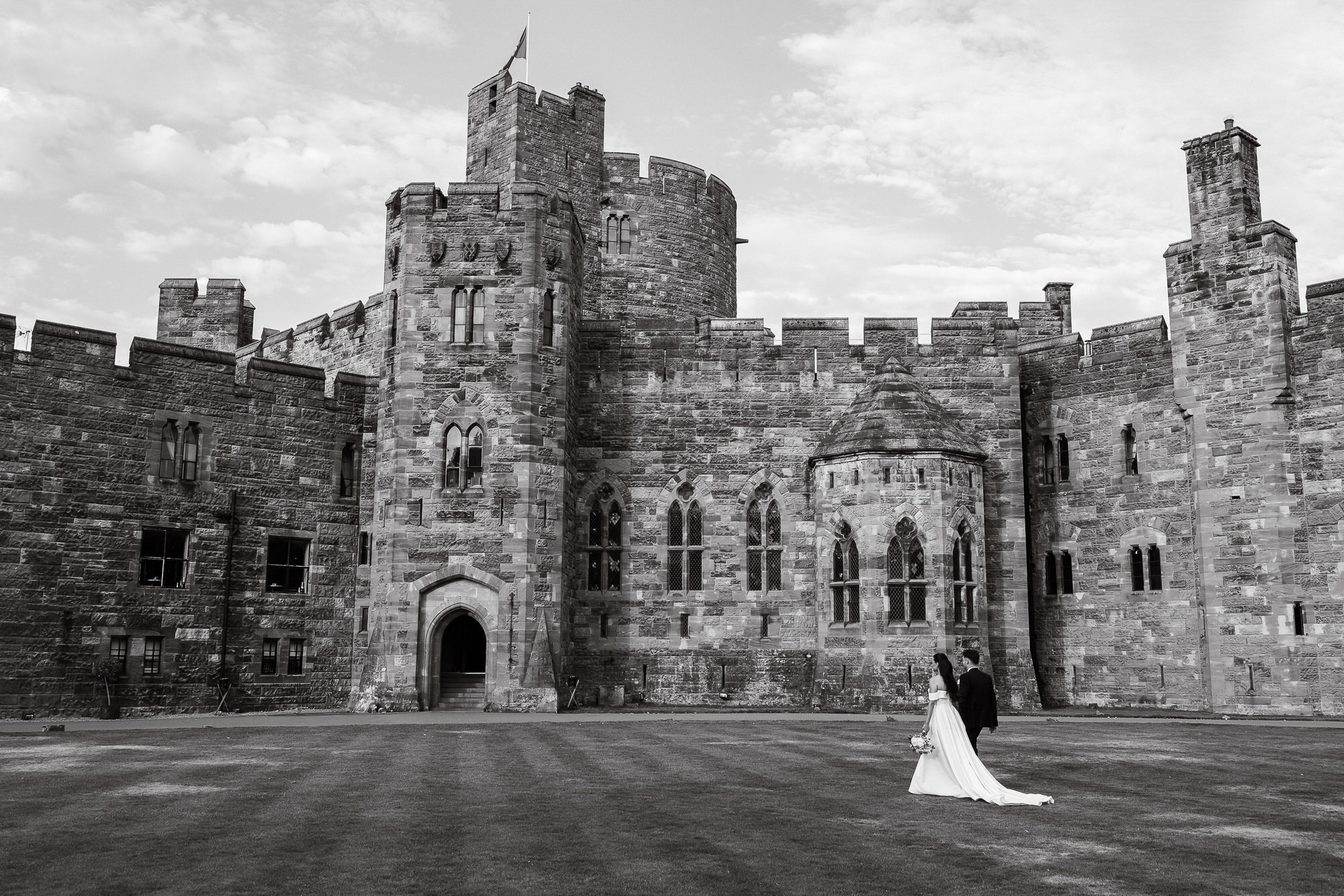 brides and groom walk across grass at the front of Peckforton Castle in Tarporley, Cheshire