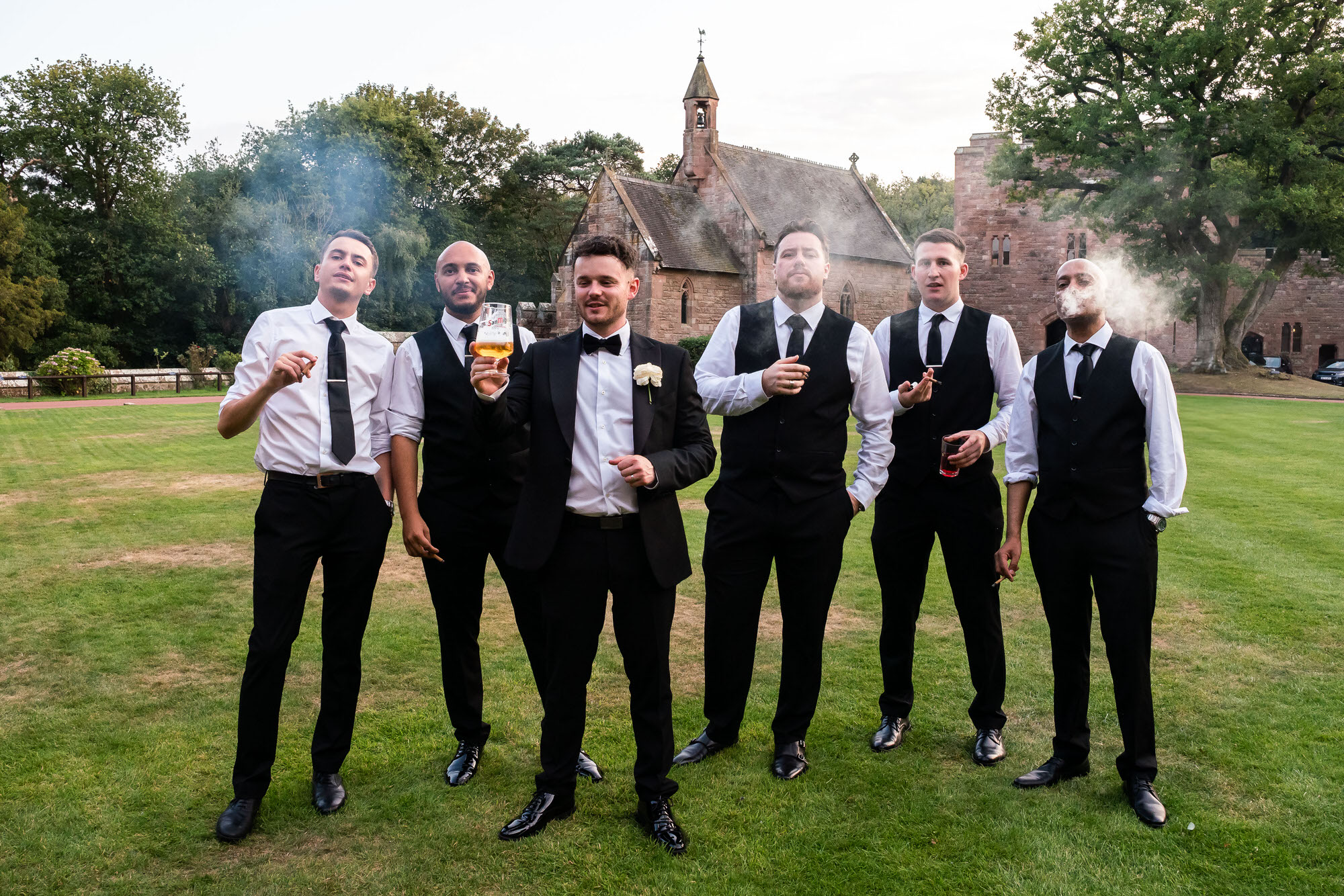 groomsmen smoke cigars outside at Peckforton Castle in Cheshire