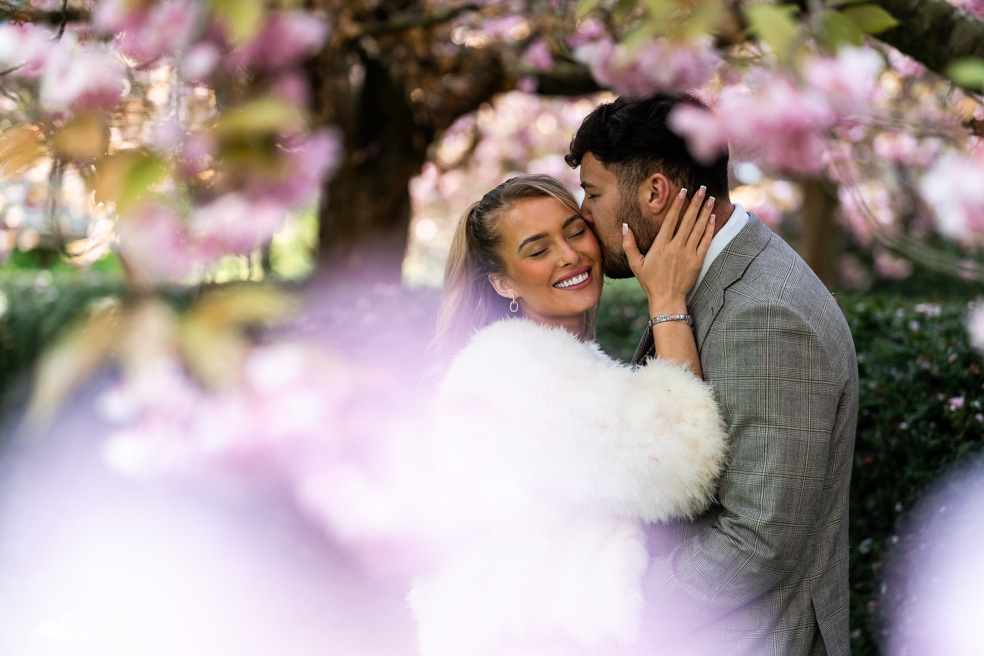 couple surrounded by blossom as groom kisses his bride on the cheek