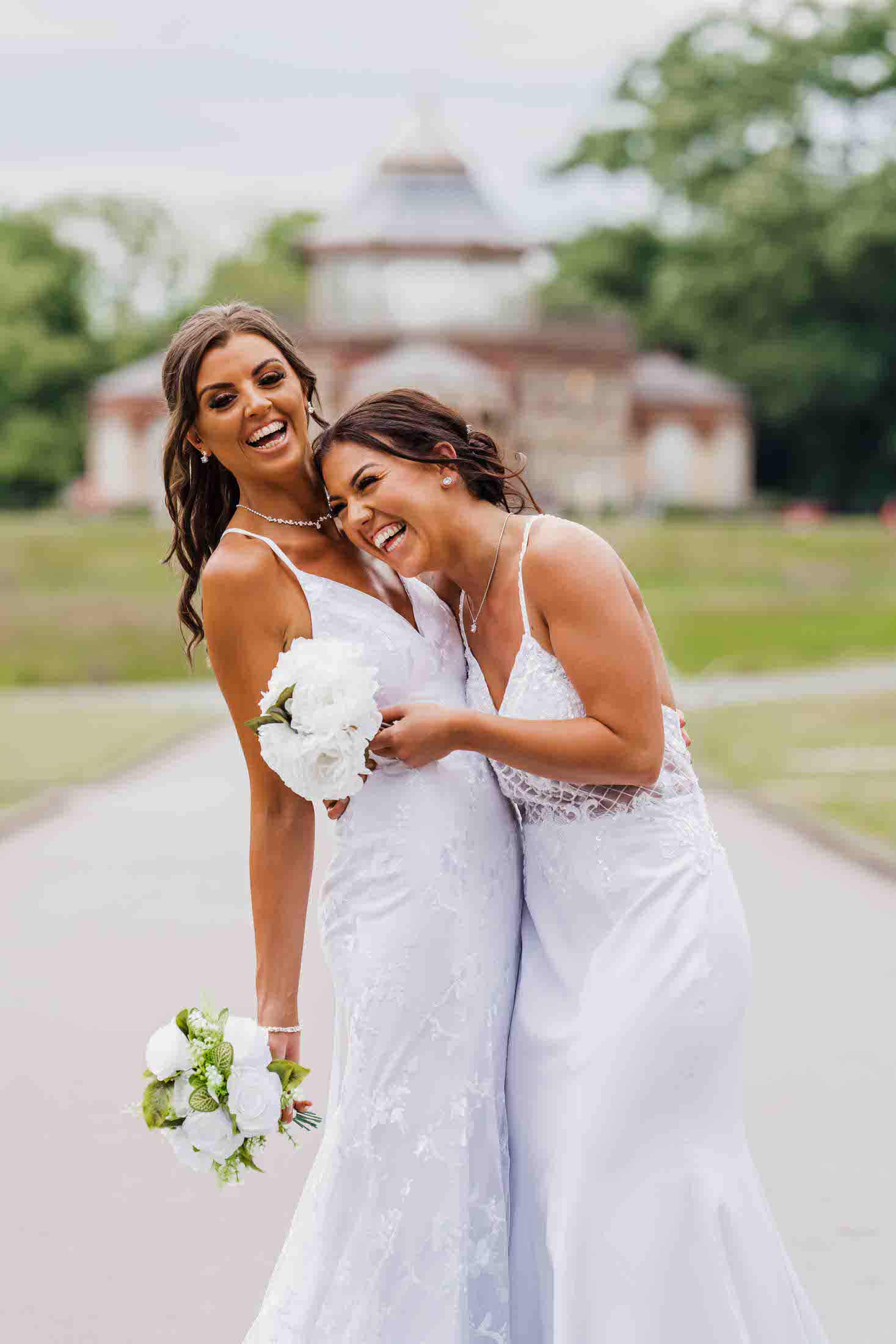 brides laugh together during couples photos just after their wedding in mesnes park, wigan